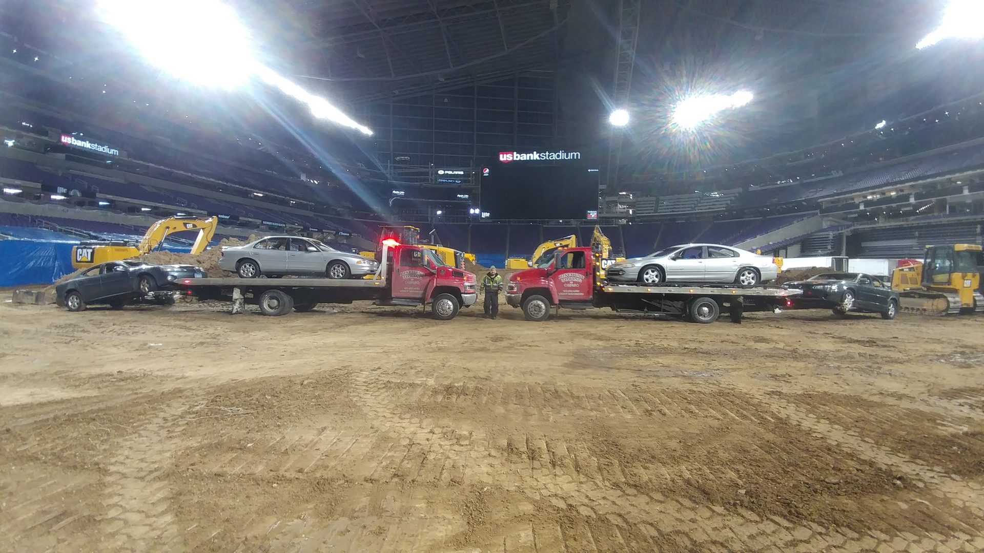 A row of red Discount Towing of MPLS flatbed trucks parked inside a stadium, each carrying a car on its deck