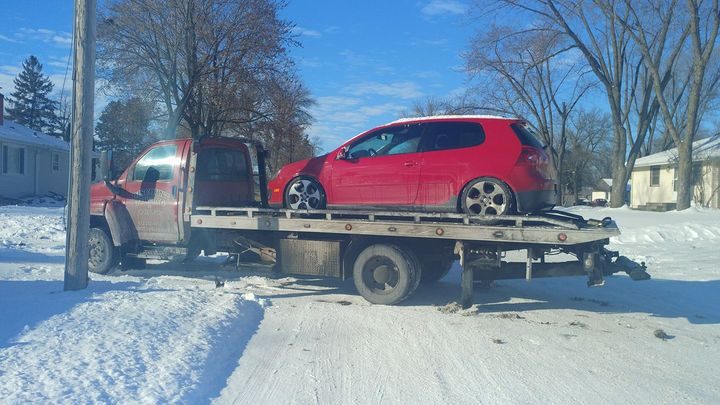 A red flatbed tow truck carrying a red hatchback on a snow-covered street in winter